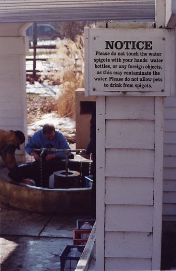 People collecting water; sign warning against touching taps